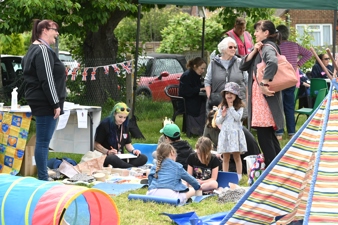 A family chatting at a community fun day. Two children doing arts and crafts while sitting on the grass.