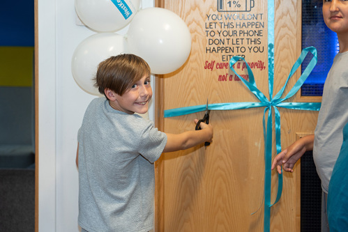 A young boy smiling while cutting a ribbon on a door with scissors